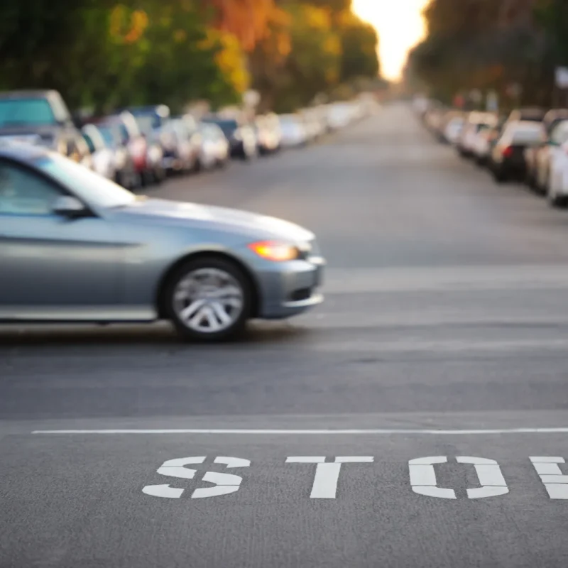 A silver sedan blurred in motion crossing a street with the word STOP painted on the asphalt in the foreground.