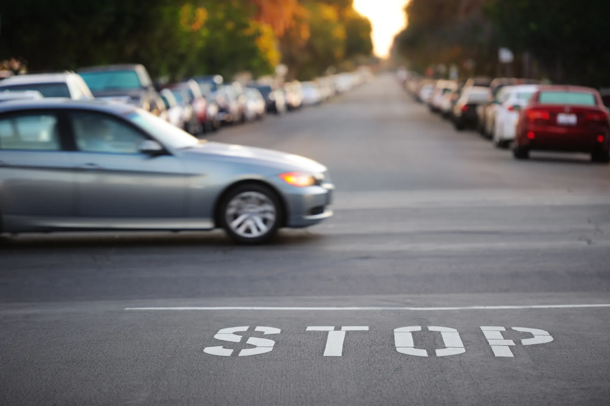 A silver sedan blurred in motion crossing a street with the word STOP painted on the asphalt in the foreground.